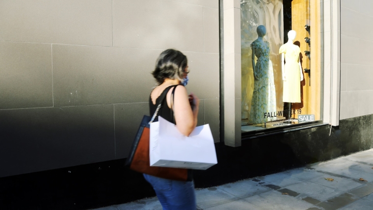 Woman walks past designer window display with shopping bag.
