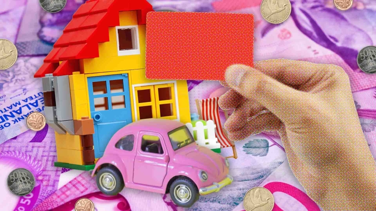 A composite image of New Zealand money overlayed with a miniature house, car and chair, and a hand is holding a red card.