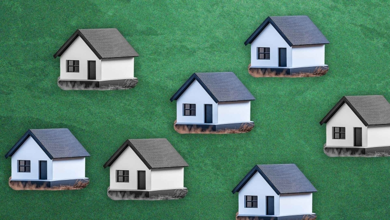A composite image of a green, textured background overlayed with miniature houses - some in colour and others in black and white. 