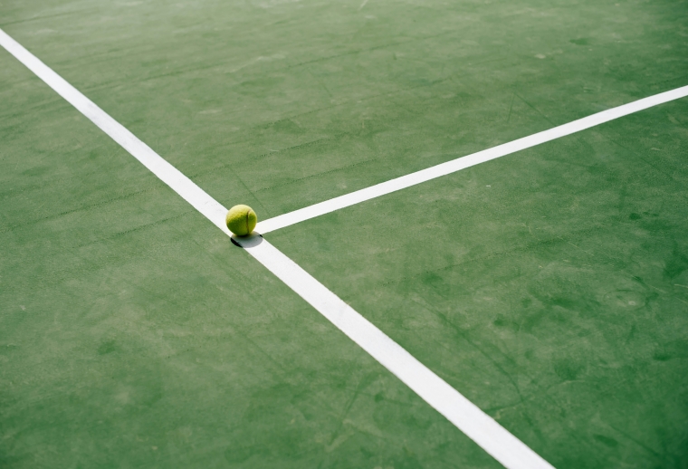 A tennis ball sits on the edge of a tennis court