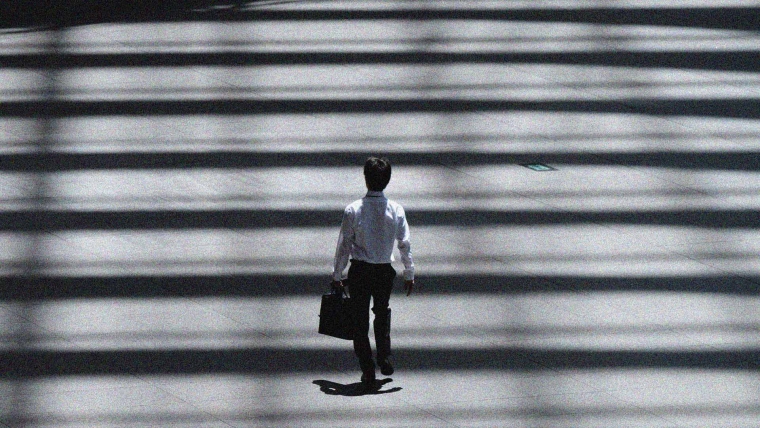 A person walking while carrying a briefcase through a zebra crossing made of lights and shadows.