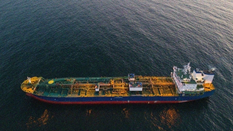 A majestic oil tanker glides smoothly across the shimmering ocean waters, its hull glistening in the warm hues of a setting sun.