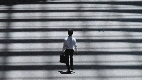A person walking while carrying a briefcase through a zebra crossing made of lights and shadows.
